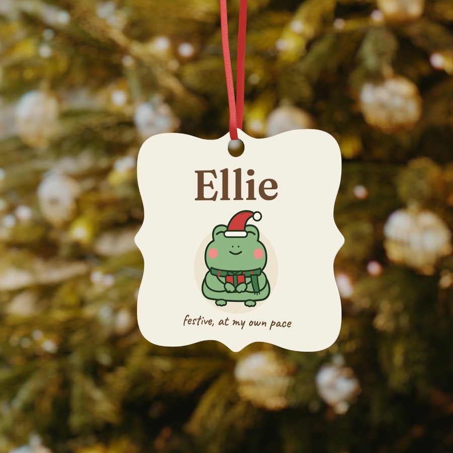 Square scalloped ornament hanging on a Christmas tree, printed Ellie above the Christmas frog
